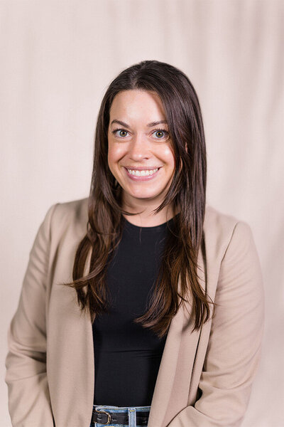 A professional headshot of Emily Austin, LCSW, smiling at the camera in a black shirt and beige blazer, representing her expertise in therapy.