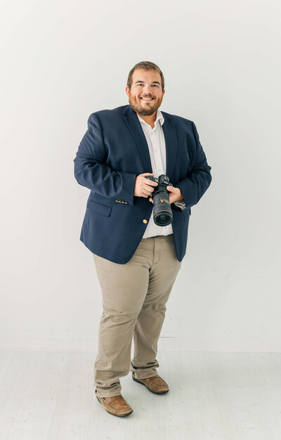 Hunter standing in a blue dress coat holding camera and smiling