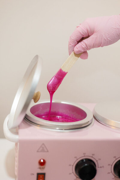 Licensed esthetician Macayla Hopper holding wax stick over wax warmer during body waxing prep in Hartselle studio