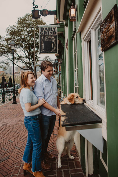 A couple standing at the window of an outdoor stand with their dog standing up next to them 