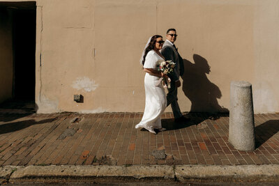 Bride and groom walking down brick sidewalk in the sun