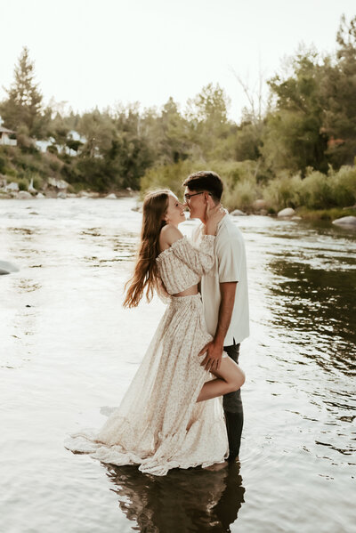 A couple standing close and going in for a kiss while standing in the river.