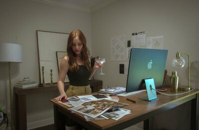 A Showit Design Partner stands at a desk with papers, magazines, and a drink in hand, looking down at documents in her modern home office—perfectly capturing the creative energy behind branding and website design.