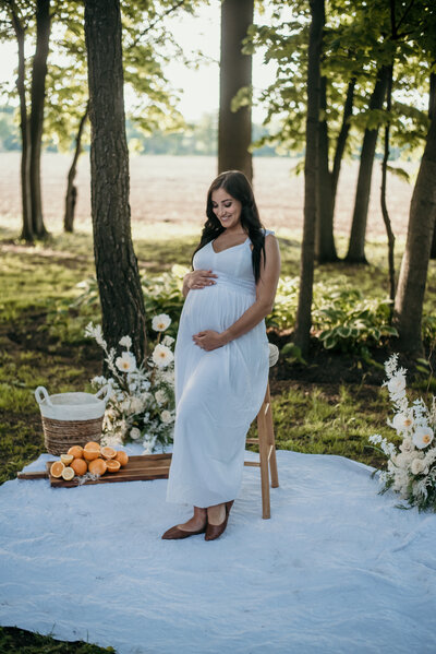 Pregnant woman holding her tummy in maternity photoshoot outside with oranges and flowers on the ground