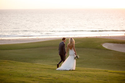 Newly married couple walking hand-in-hand along beachside golf course