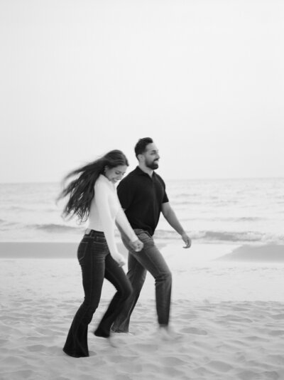 candid black and white movement photography, couple running on beach, film engagement photos in Northern Michigan