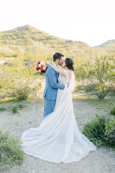 Newlyweds embrace and kiss in the midst of the desert, adorned in beautiful attire