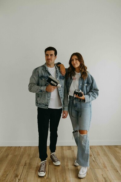 Close-up of Alberta photographer and videographer duo Hannah and Tyler holding a digital camera and a Super 8 video recorder.