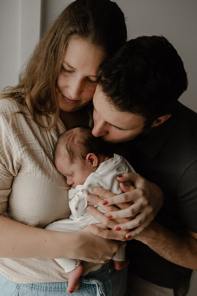 koppel geeft hun pasgeboren baby een kus op het hoofd tijfens een in-home newborn fotoshoot te Bonheiden.