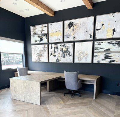 Home styling and décor service in a home office featuring a dark blue wall, artwork with gold touches, a corner desk, and a grey chair for an elegant, professional atmosphere.