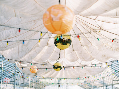 A detail of the reception decorations including colorful string lights, paper lanterns, and mirror globes, inside the greenhouses at Dos Pueblos Orchid Farm.