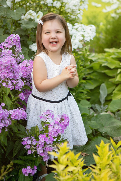 small girl standing in front of purple flowers smiling