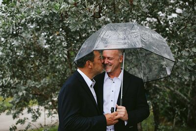 Two Grooms kissing under Umbrella on Elopement Day