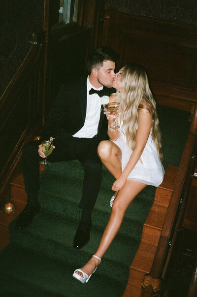 Boston bride and groom sitting on wooden stairs with green runner kissing