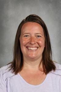 A smiling female teacher in a purple shirt, embodying positivity, gives a recommendation for Gamably.