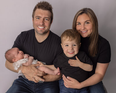 Smiling family of four during a newborn photo session in Northern NJ with parents holding their baby girl and toddler son