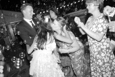 Emotional moment of the bride kissing her mother on the cheek during a joyful bubble exit at a high-end Austin wedding, captured in timeless black and white with editorial detail.