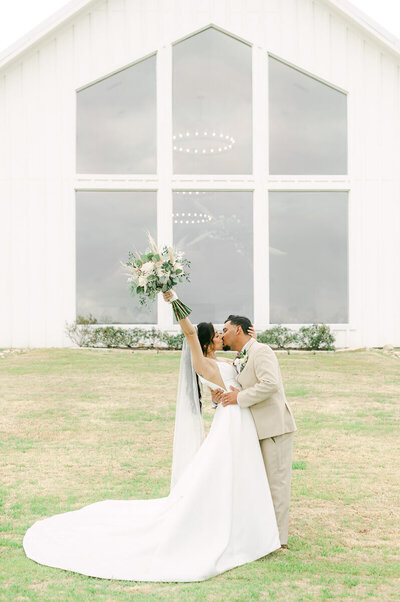 bride and groom kissing behind the farmhouse wedding venue