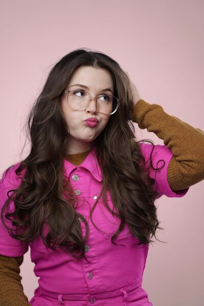Photographer Lana Stewart poses in cute authentic headshot wearing pink jumpsuit and pursing lips looking to the right