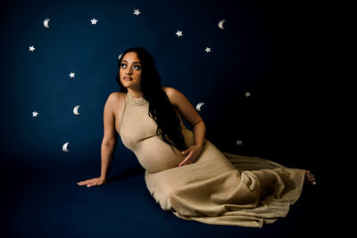 Connecticut maternity photographer creates celestial studio portrait of pregnant woman in gold gown against starry night backdrop