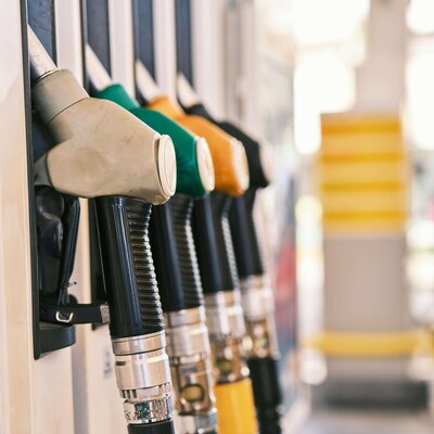 A close-up of a row of colorful gas pump nozzles, arranged in yellow, green, and black, at a fuel station under soft lighting.