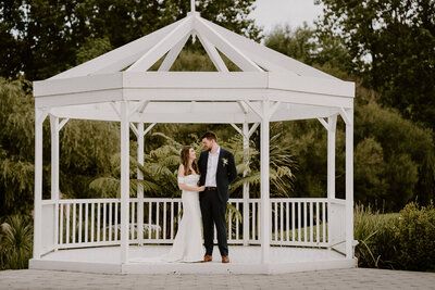 Newlyweds stand under an archway in a garden at Abel Estate in Kumeu, Auckland.