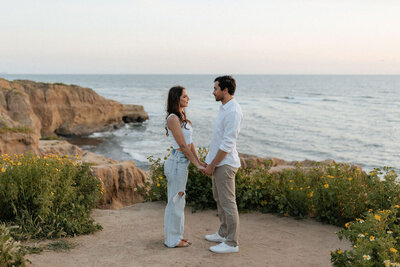 Couple holding hands on the cliffside with yellow flowers.