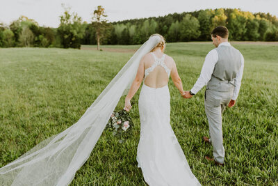 Bride and groom walking hand-in-hand through a peaceful field, their backs to the camera, as they prepare for a Christ-centered wedding day full of love and joy.