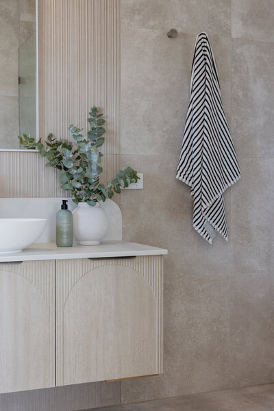 Modern bathroom with a striped towel on the wall, eucalyptus in a vase, and a soap dispenser on the counter—an exquisite example of bespoke interior design in Newcastle NSW.