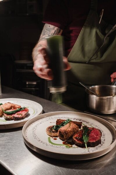 Chef garnishing a gourmet meat dish with green sauce in the kitchen of Sael Birmingham restaurant.