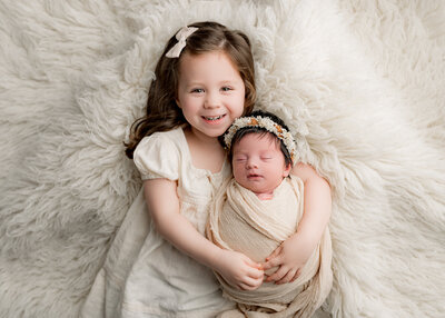 big sister wearing a bow in her hair holding her newborn sister wearing a flower crown