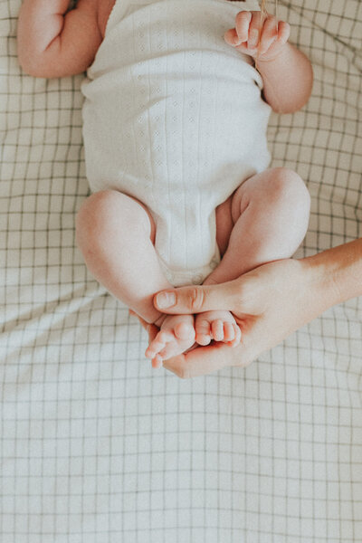 photo of mom holding her babies feet while they are laying on a bed taken in langley