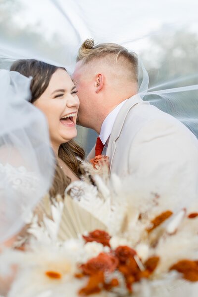 Close up of bride sitting in front of wildflowers, one hand on knees, one hand in her hair