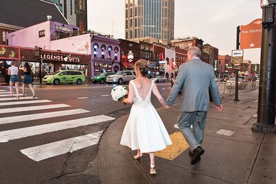 Couple holding hands walking on Broadway in Nashville after eloping on the Pedestrian Bridge