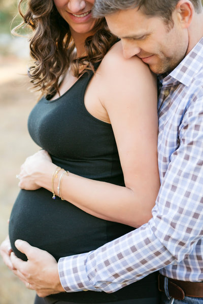 Expecting Denver couple pose for photo. Husband is hugging  the baby bump