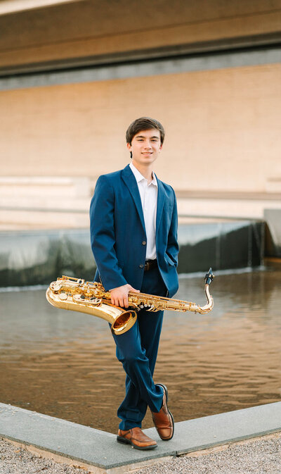 Boy in a suit, holding a saxophone, smiling at the camera.