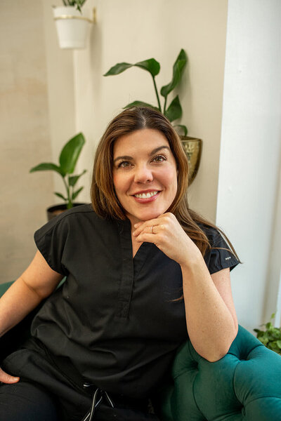 Female nurse wearing black scrubs smiling with hand on chin