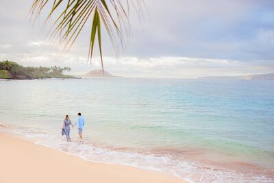 couple walking hand in hand down a Maui beach during their engagement photoshoot