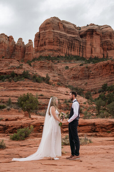Bride and groom holding hands during an emotional elopement ceremony at Cathedral Rock in Sedona, Arizona, surrounded by red rock cliffs.