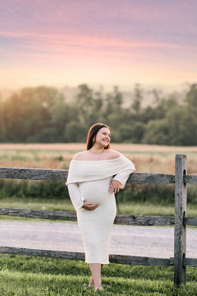 pregnant woman in white dress standing by a wooden fence at sunset near York, PA

