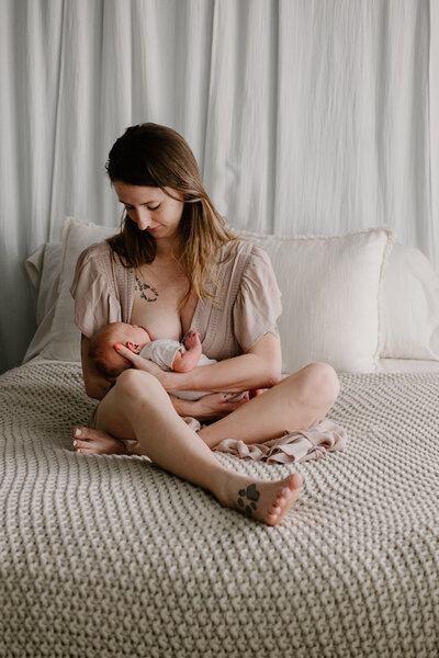 Mom wearing beige dress breastfeeding newborn baby girl in lifestyle studio in Severn Maryland.