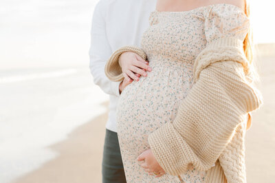 Beautiful creamy colors and cozy sweater of mom and dad holding belly closeup
