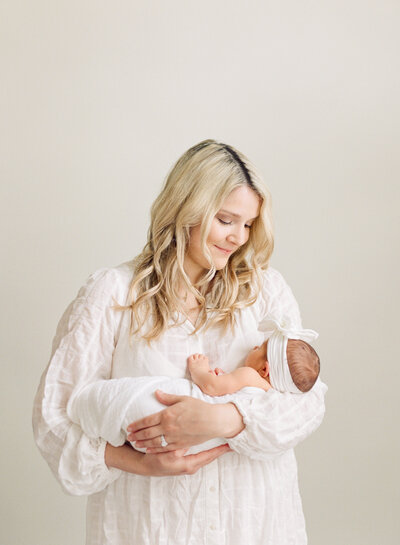 Mom holding newborn baby and smiling at him while he holds her finger during their newborn photography session in Raleigh NC. Photographed by Raleigh Newborn photographers A.J. Dunlap Photography.