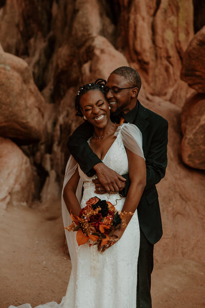 photo of groom embracing bride from behind while they both smile with red rock formations in the background taken by Elopement photographer in breckenridge
