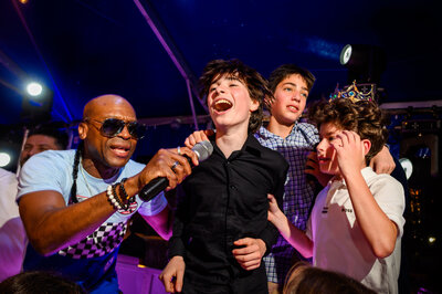 Lively interaction at a Bar Mitzvah celebration as a boy takes the stage with a microphone, sharing a fun moment with an entertainer and his friends
