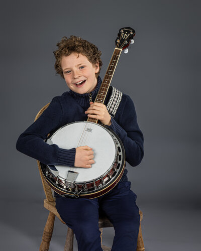 A boy sitting on a chair with a banjo