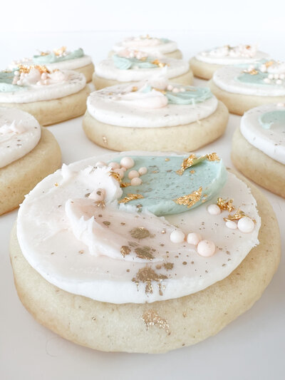 Buttercream sugar cookie topped with white and blue frosting, gold dust and sprinkles.