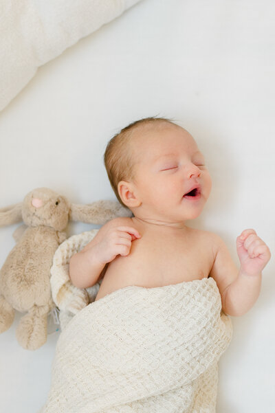 Newborn baby sleeping next to his baby bunny in his crib during a lifestyle newborn session