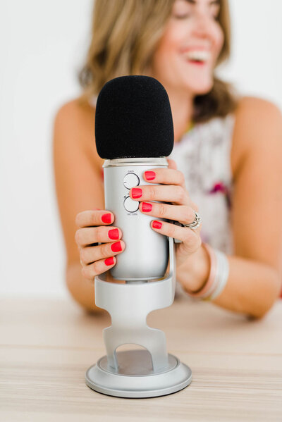 smiling woman with hands on a podcast mic with red fingernails