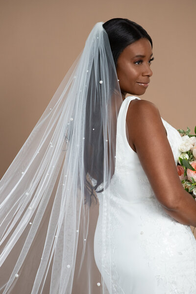 Bride wearing a veil with big pearls and holding a bouquet